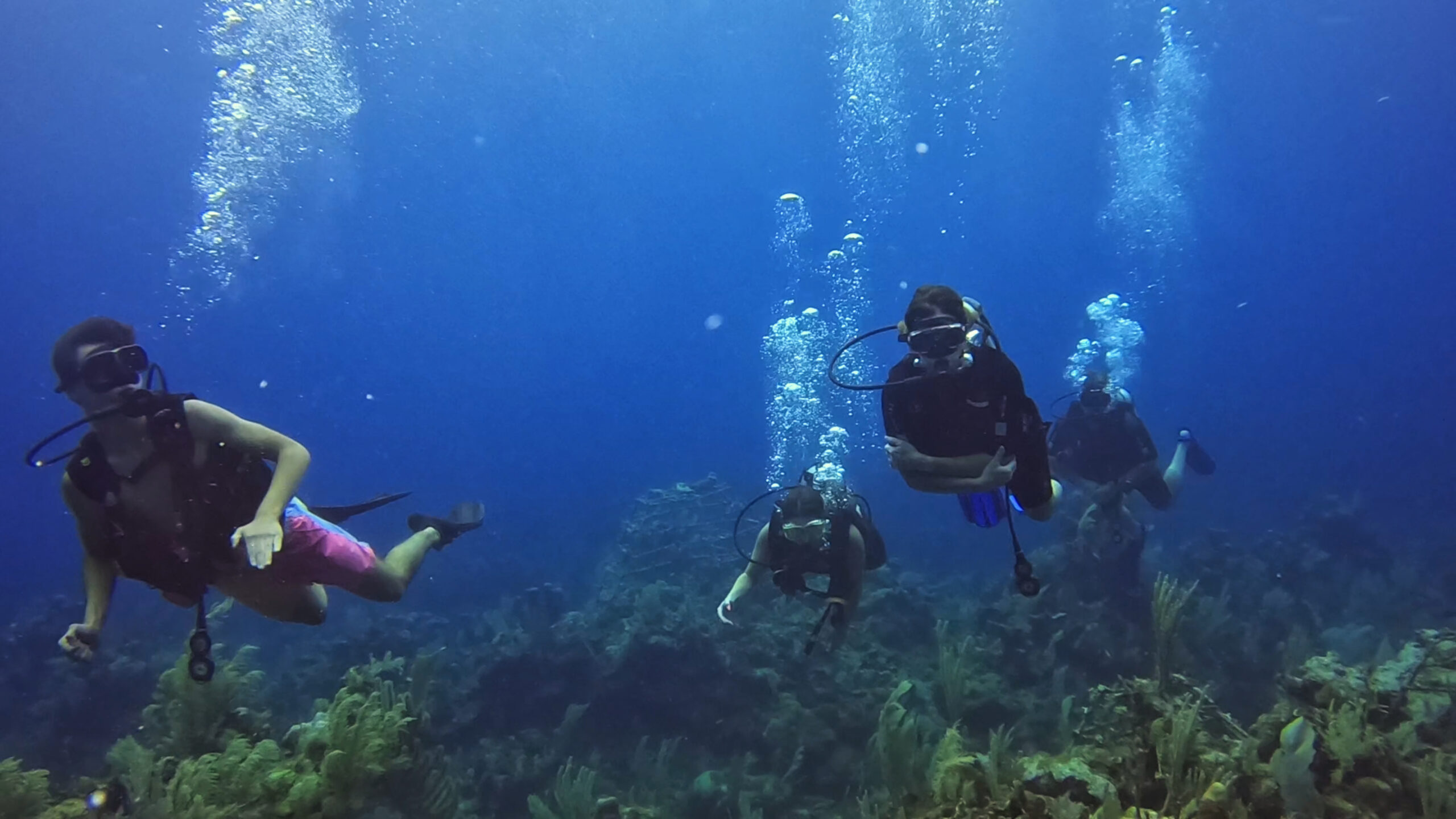 Family scuba diving together over a coral reef in Roatan
